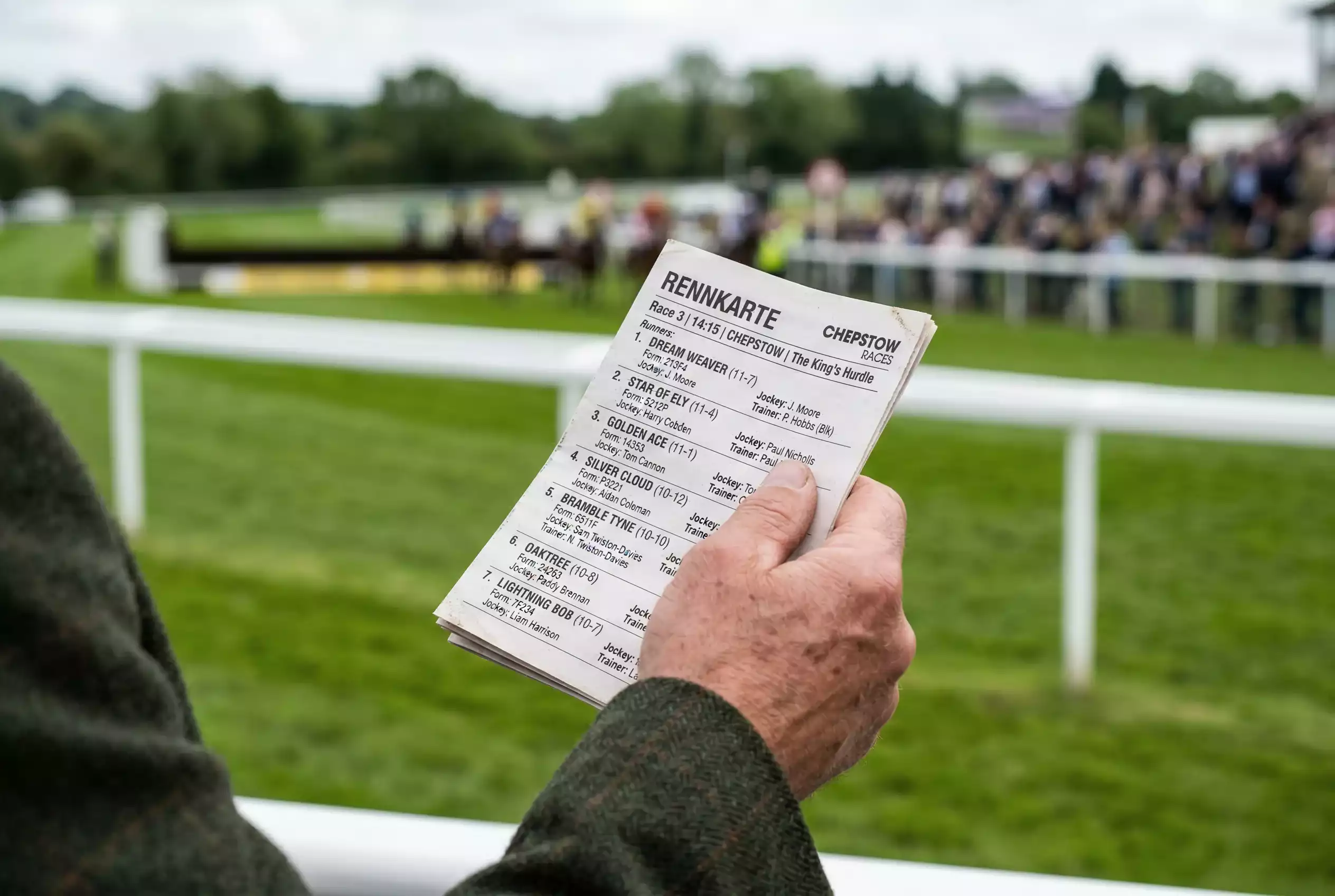Rennkarte lesen — Nahaufnahme einer Hand, die eine gedruckte Rennkarte mit Formzahlen und Starterfeld hält, unscharfe Rennbahn im Hintergrund